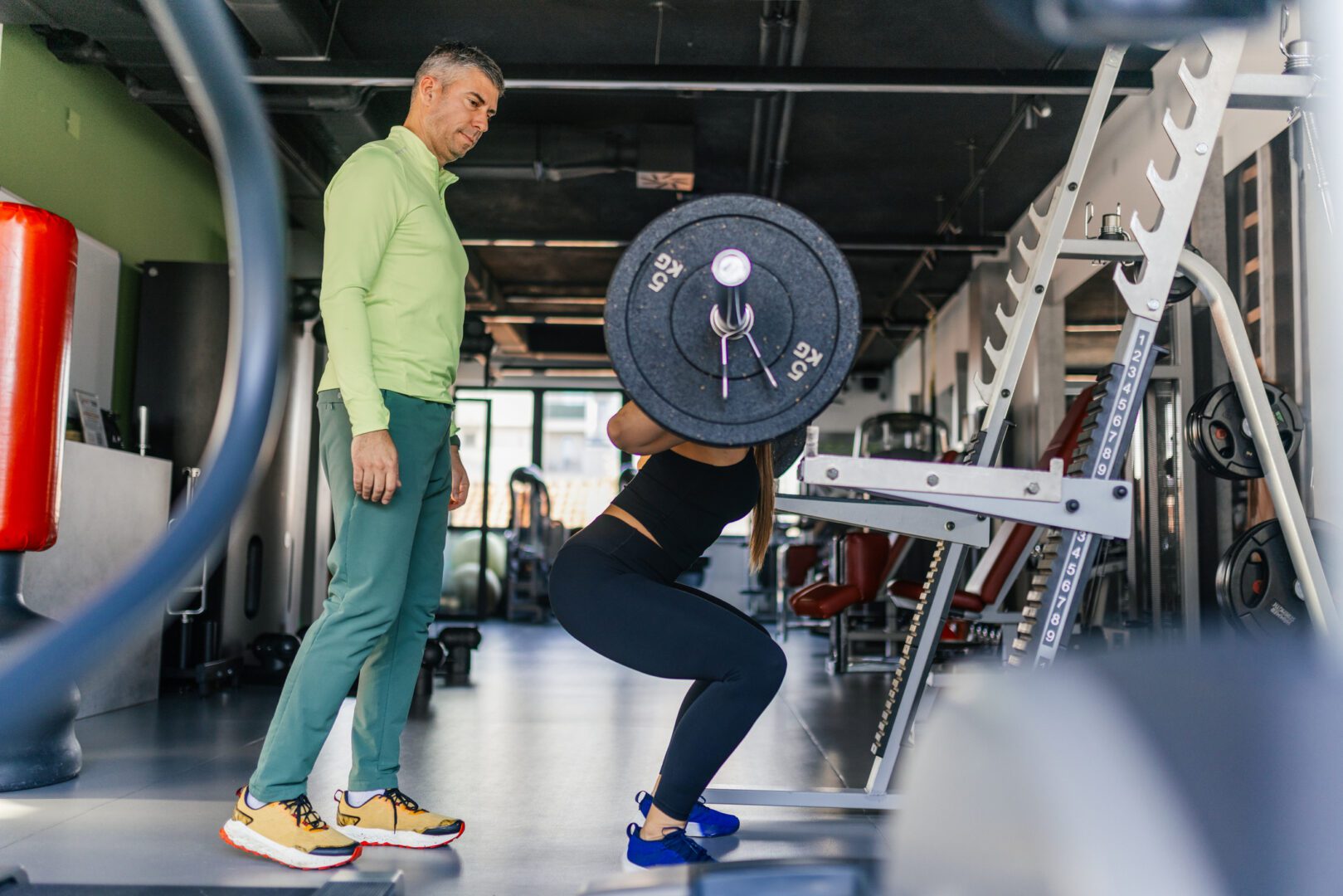 Personal trainer spotting woman performing barbell squat